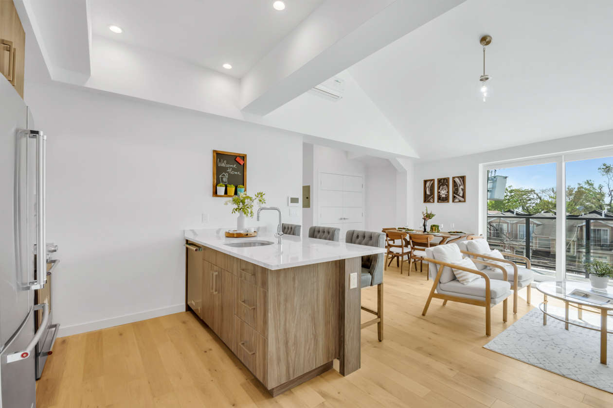 Bright open kitchen and living room with wooden floor, kitchen island, dining table, and large sliding glass doors.