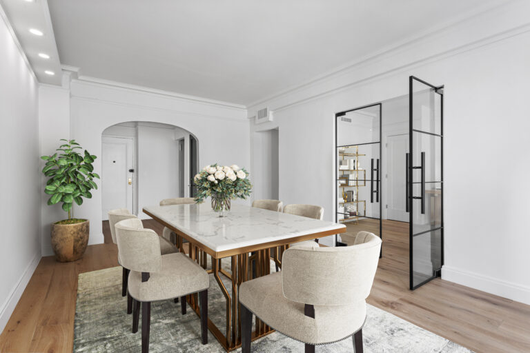 Modern dining room with a marble-top table, beige upholstered chairs, a centerpiece of white flowers, a potted plant, and glass double doors.