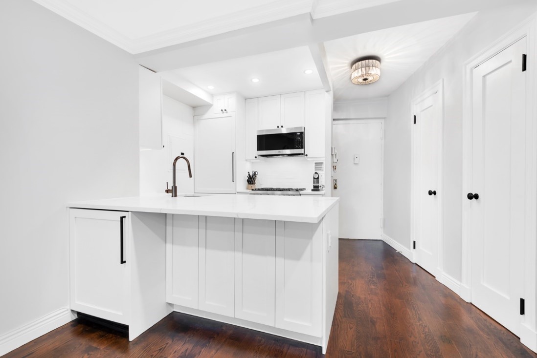 Bright modern kitchen with white cabinets, marble countertop island, stainless steel microwave, and dark wood flooring.