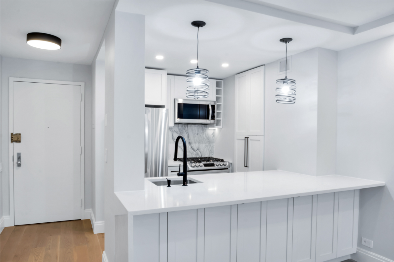 Modern white kitchen with marble backsplash, stainless steel appliances, black faucet, and spiral pendant lights above a large countertop.