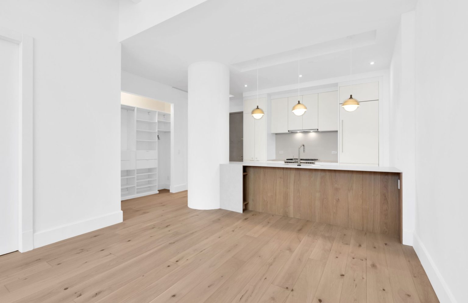 Modern open kitchen with white cabinets, wooden island, three pendant lights, and light wood flooring.