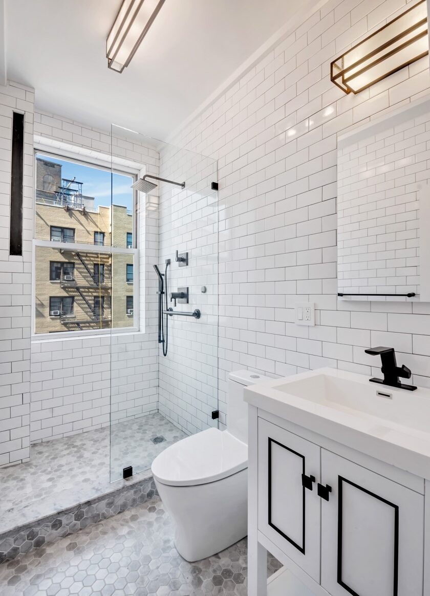 Modern bathroom with white subway tile walls, glass-enclosed shower, white toilet, and white vanity with black faucet and cabinet accents.