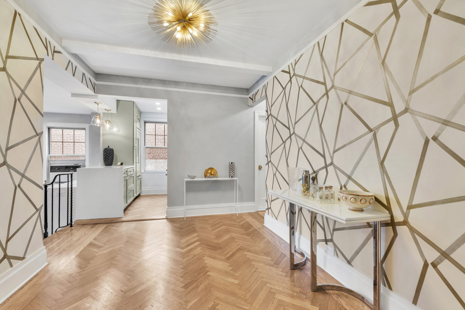 Modern entryway with geometric patterned walls, wooden herringbone floor, and a slim white console table topped with decorative items.