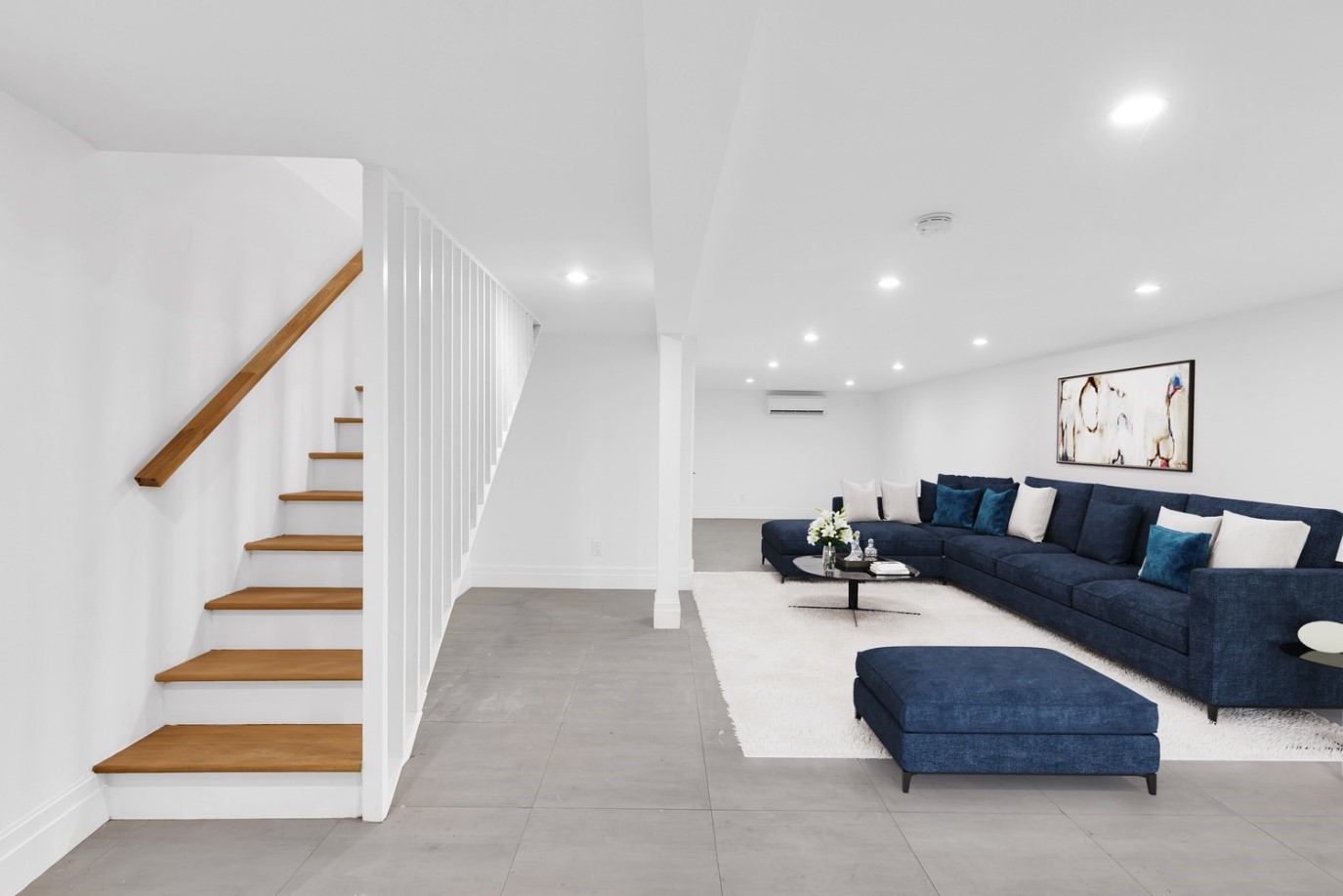 Modern basement living area with wooden stairs, blue sectional sofa, white rug, and abstract wall art.