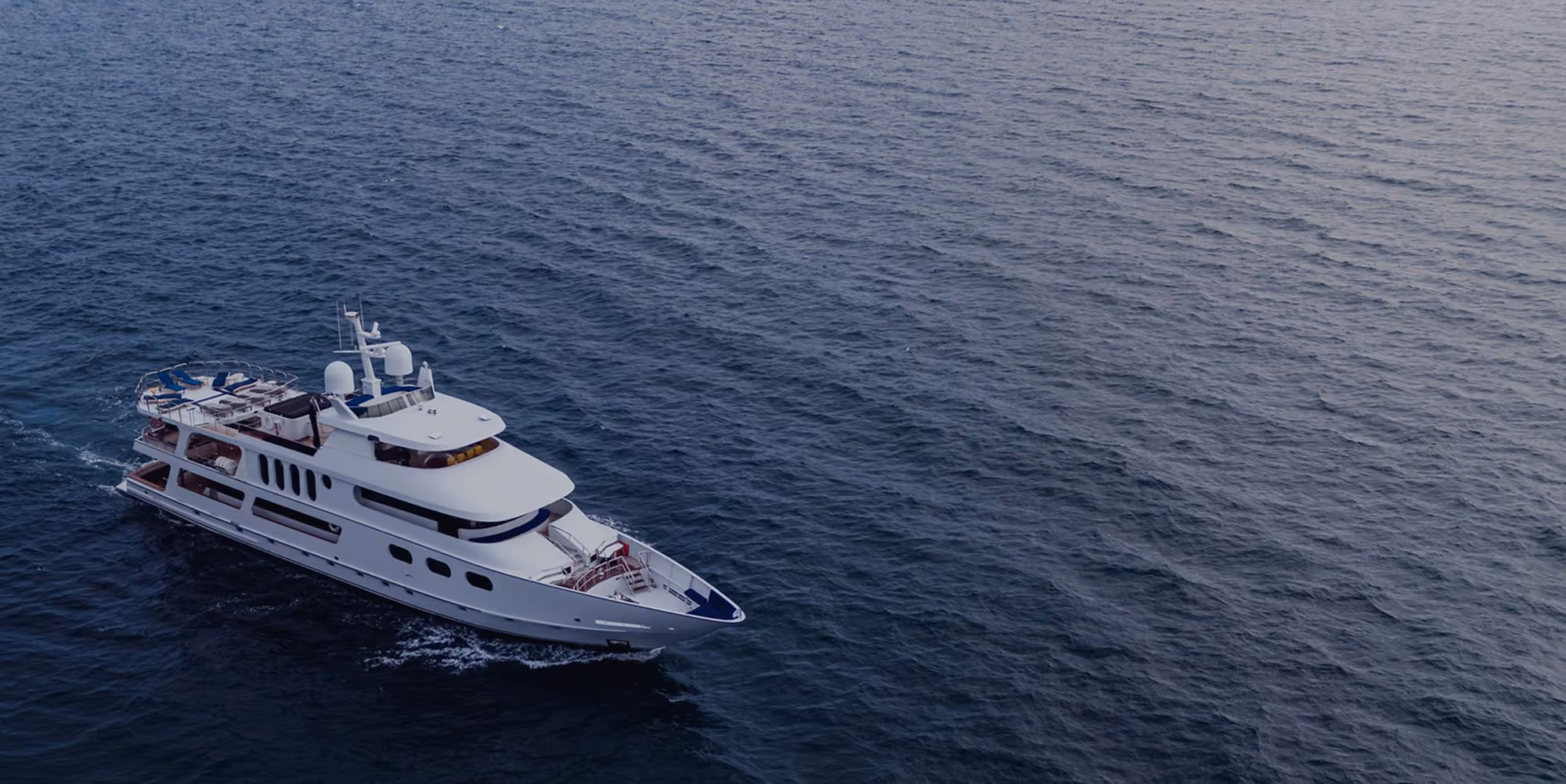 White luxury yacht cruising on calm ocean waters viewed from above.