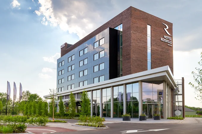 Modern Hotel Rosveld building with glass windows and brick facade under a partly cloudy sky.