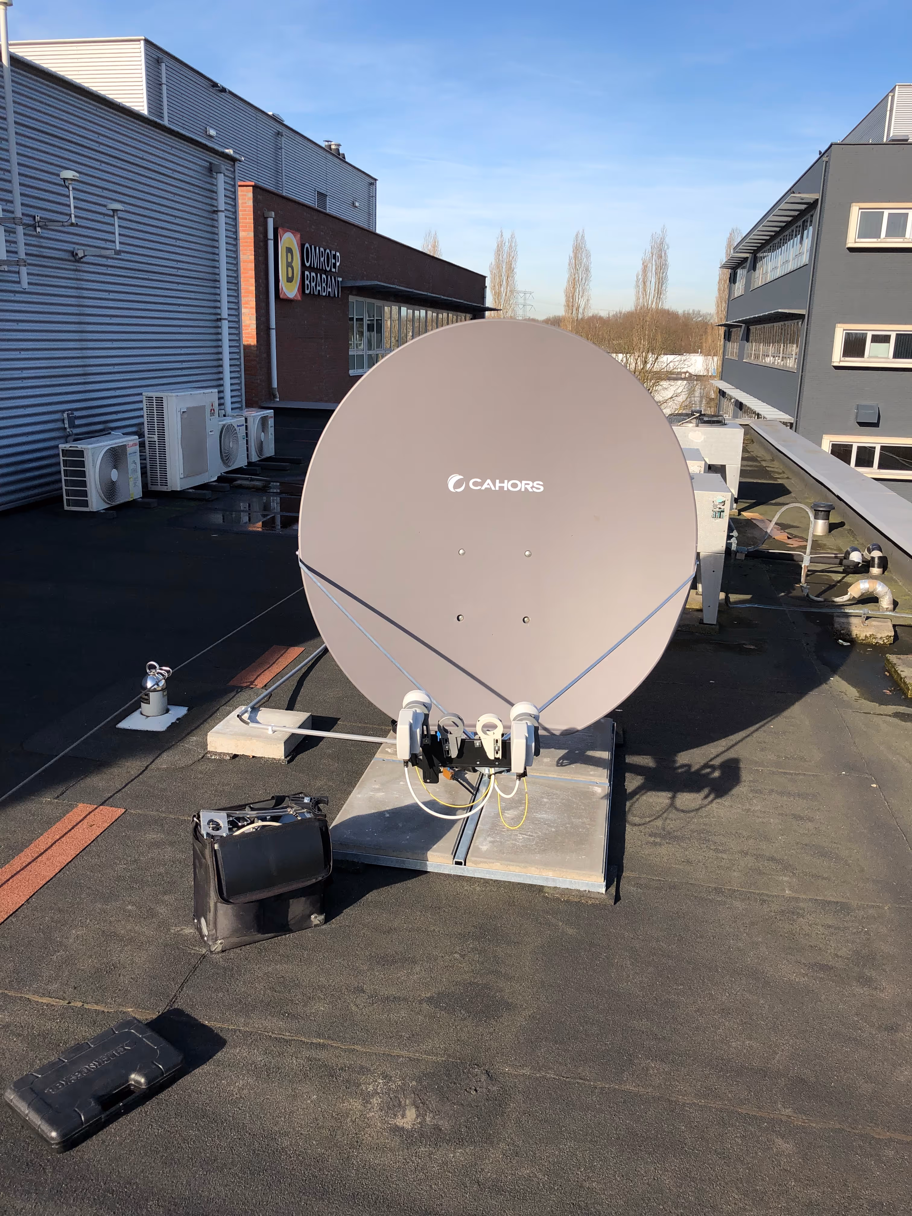 Large Cahors satellite dish on a rooftop with buildings and air conditioning units in the background.