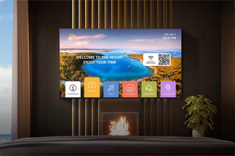 Modern hotel room with a wall-mounted TV displaying a resort welcome screen over a fireplace and a potted plant.