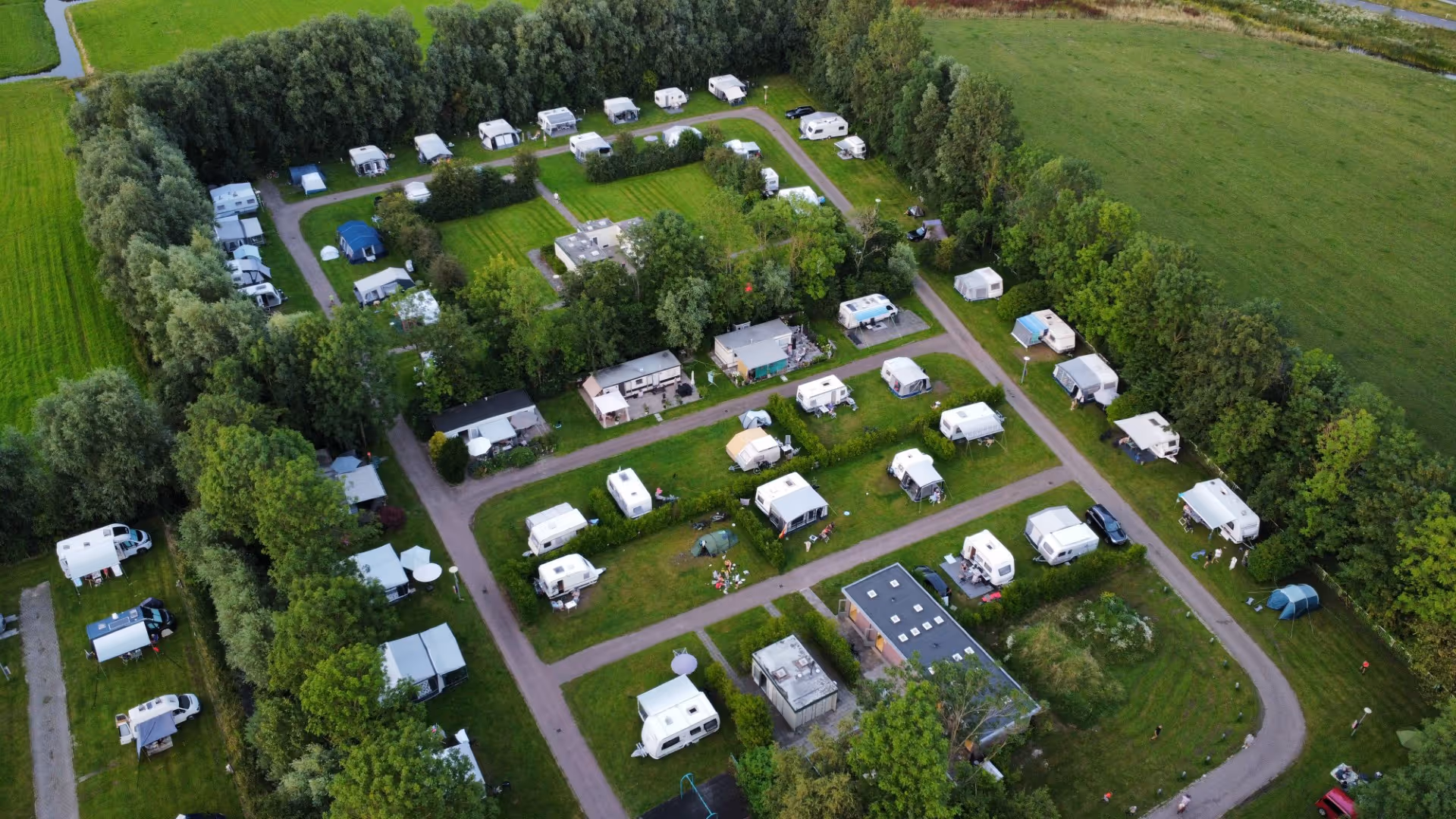 Aerial view of a green campsite with multiple RVs, caravans, tents, walkways, and trees.