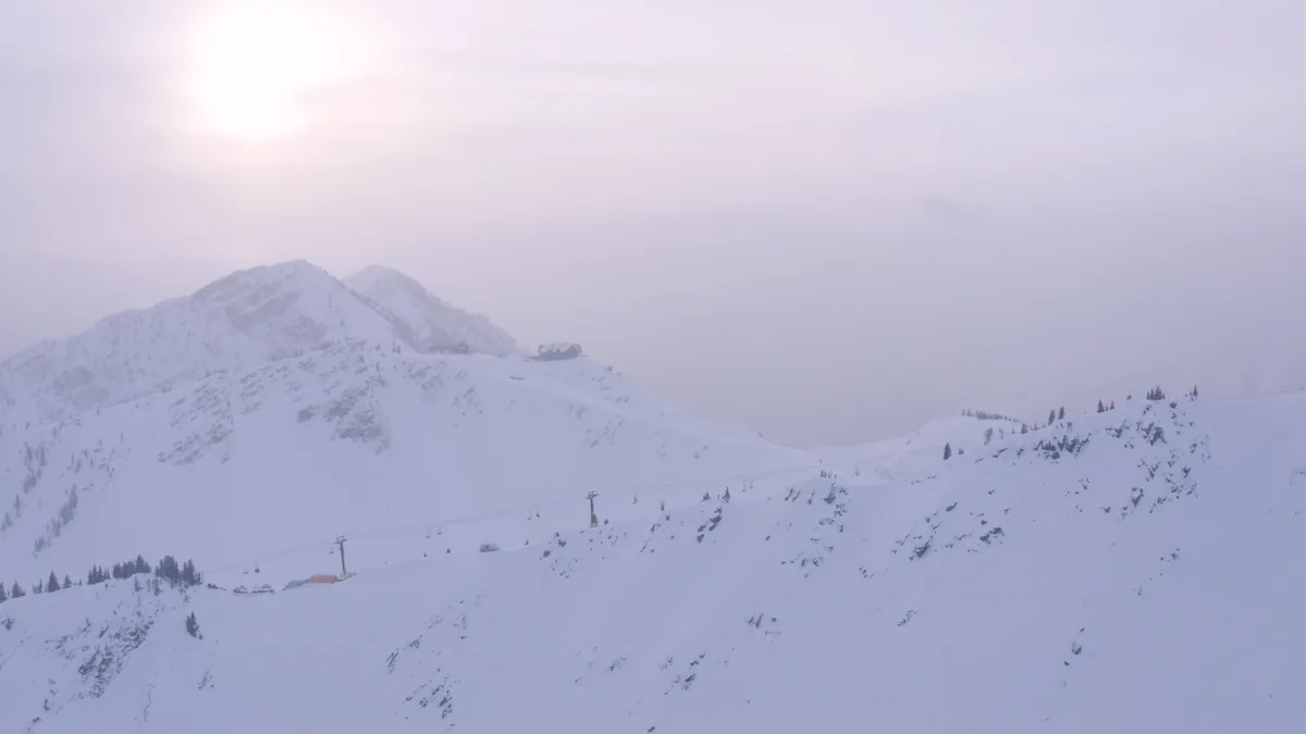 Snowy alpine terrain beneath pale winter sun and haze