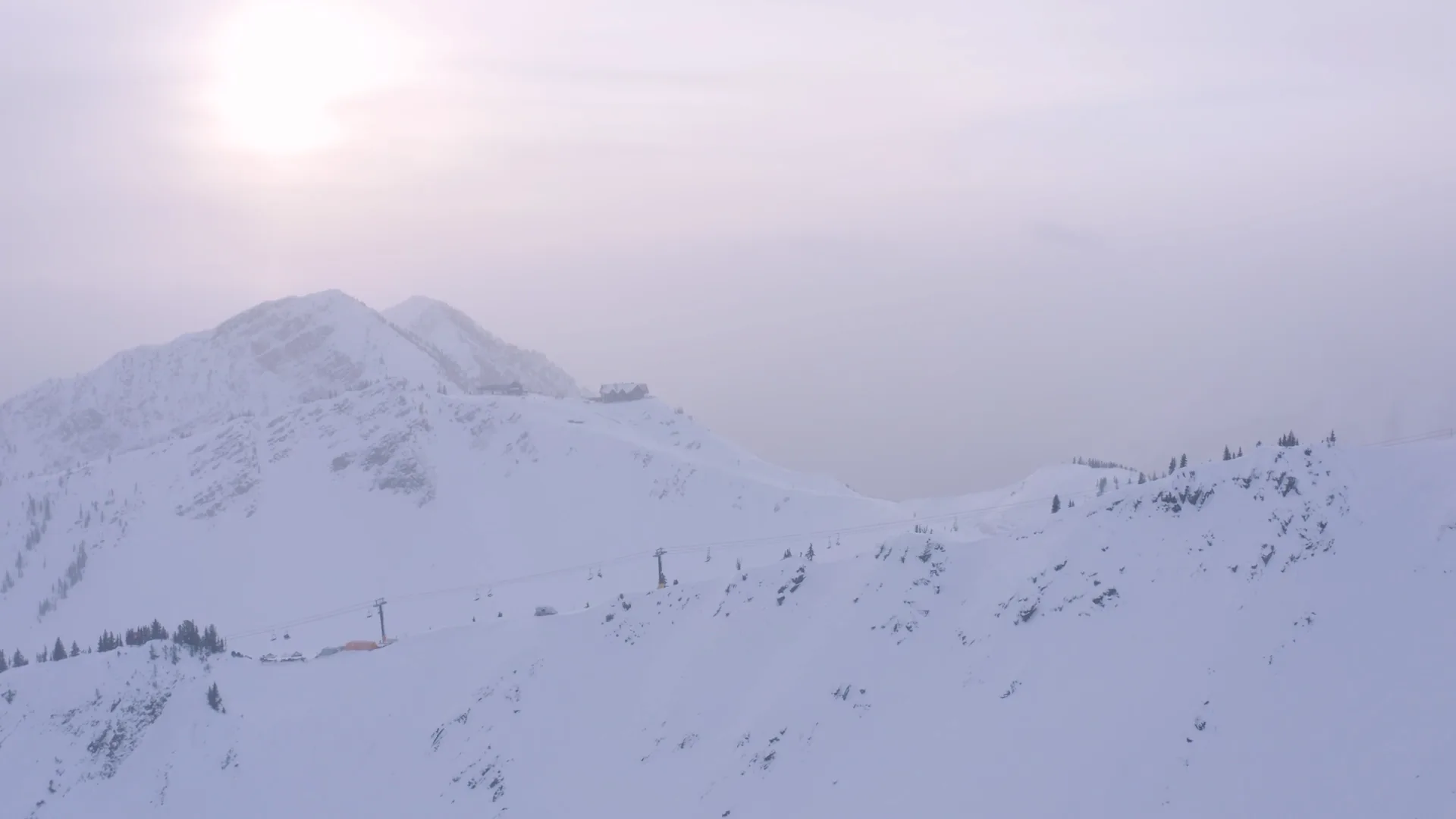 Snowy alpine terrain beneath pale winter sun and haze