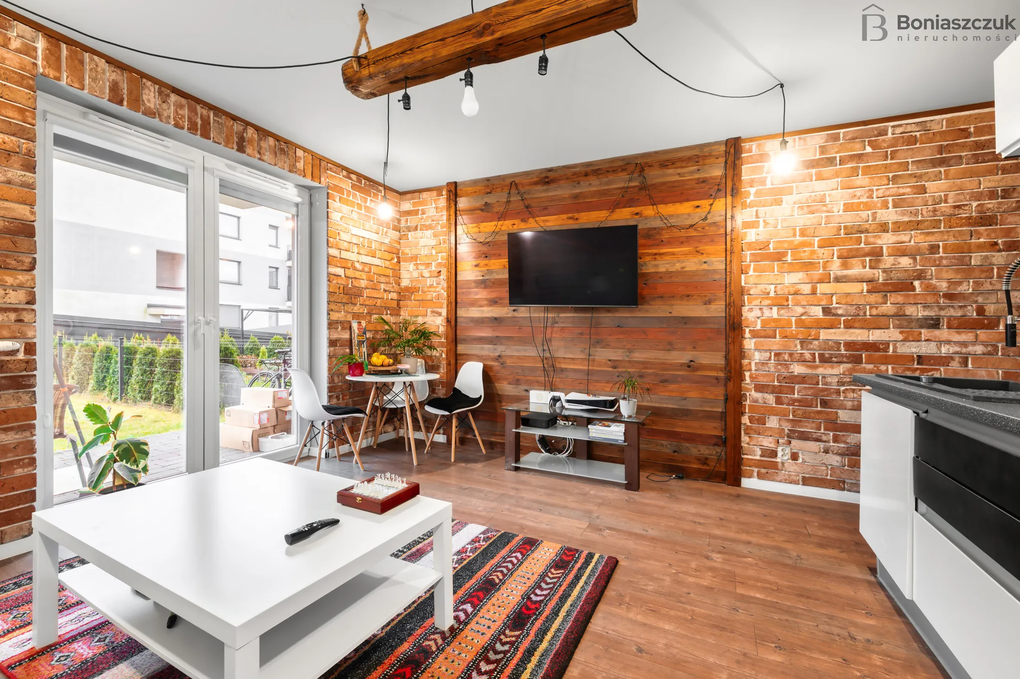 Przytulny salon z białym stolikiem, kolorowym dywanem, ceglaną ścianą i drewnianą ścianą z zawieszonym telewizorem.