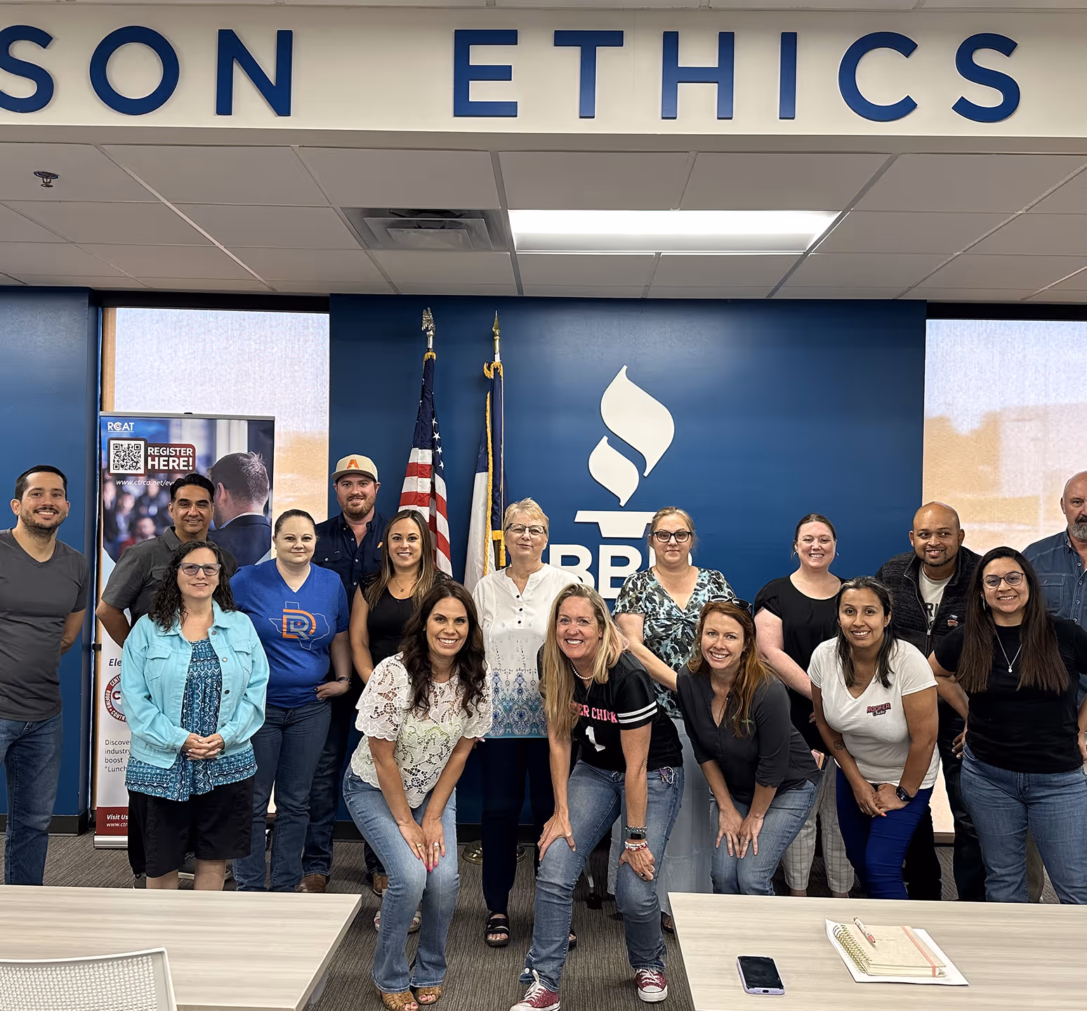 Group of smiling people posing inside a room with blue walls featuring American and Texas flags and the BBB logo.