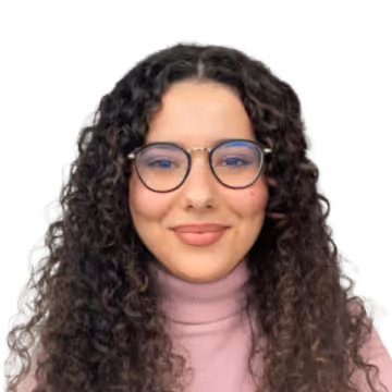 Femme souriante aux cheveux bouclés longs portant des lunettes rondes et un col roulé rose.