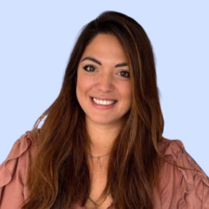 Femme souriante aux longs cheveux bruns portant un haut rose avec volants.