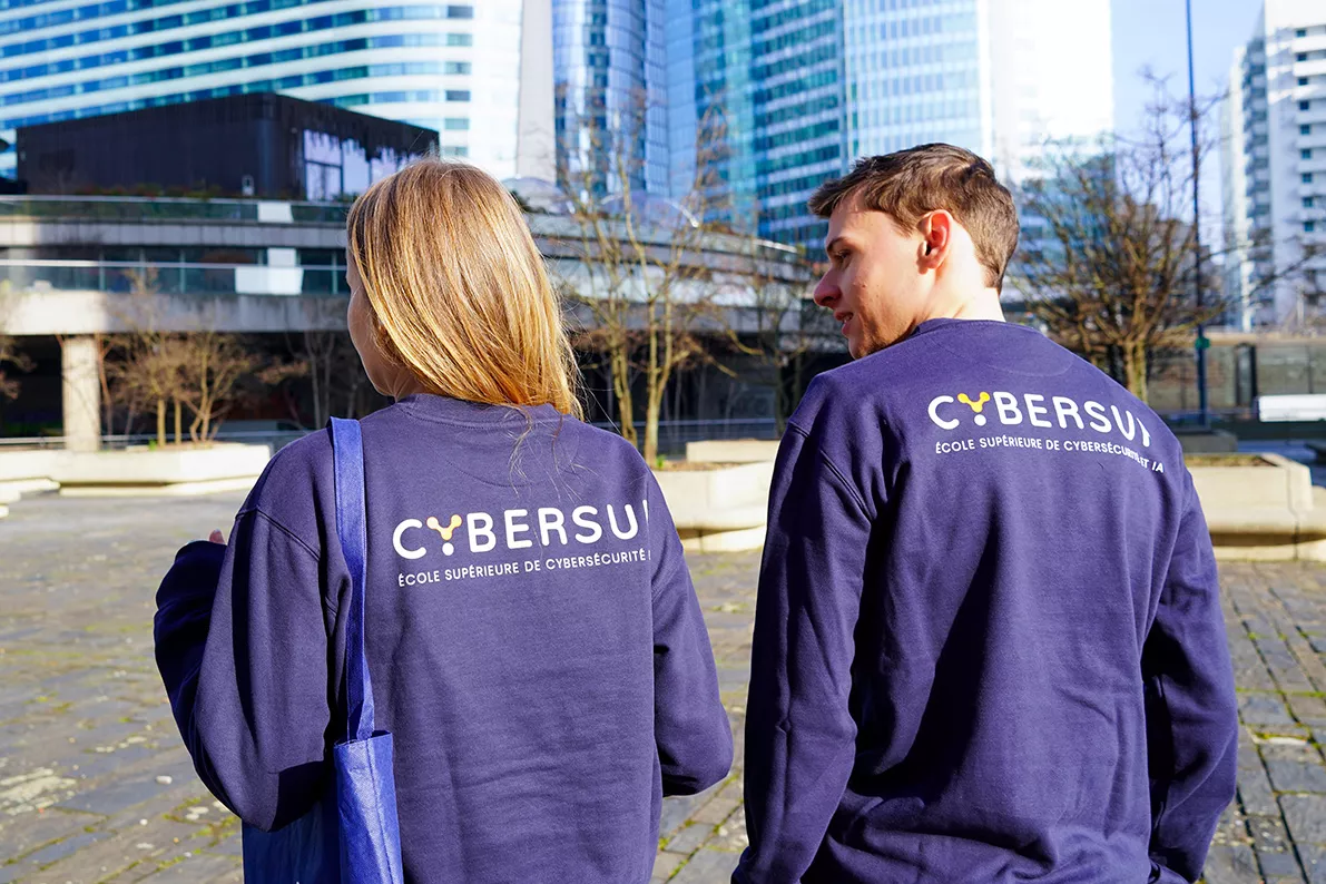 Quatre étudiants marchant ensemble dans un couloir d'école en discutant et souriant, avec des livres et un sac à dos.
