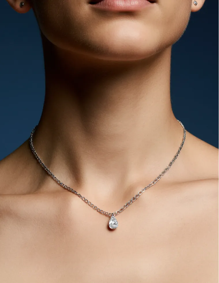 Close-up of a woman's neck wearing a silver chain necklace with a teardrop-shaped pendant.