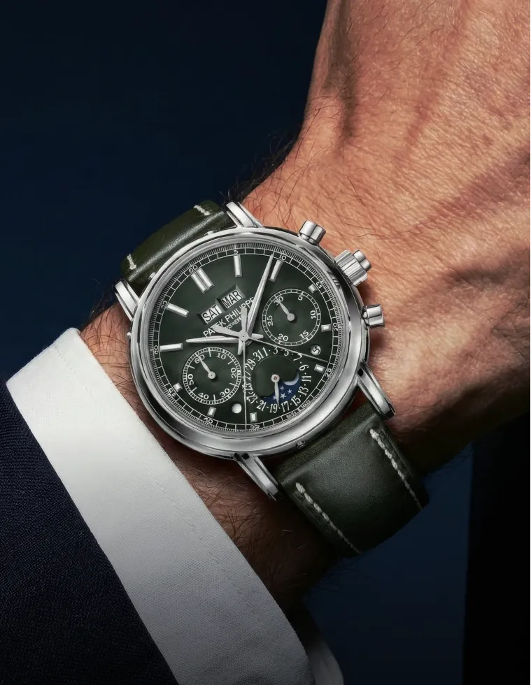 Close-up of a wrist wearing a green leather-strapped Patek Philippe watch with multiple dials and day-date display.