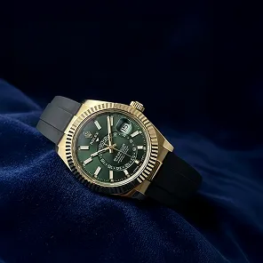 Gold analog wristwatch with a green dial and black strap resting on dark blue fabric.