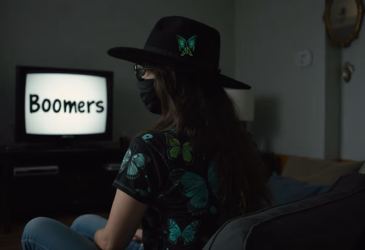 Astrid Aillume seated alone on a sofa watching a TV screen with the word Boomers.