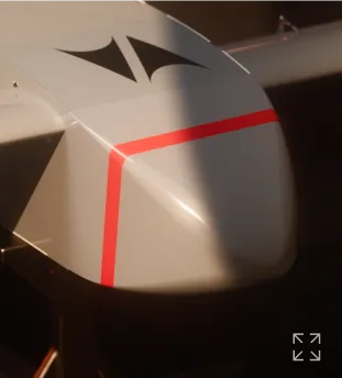 Close-up of a gray drone nose with black triangular decals and a red stripe around the tip.