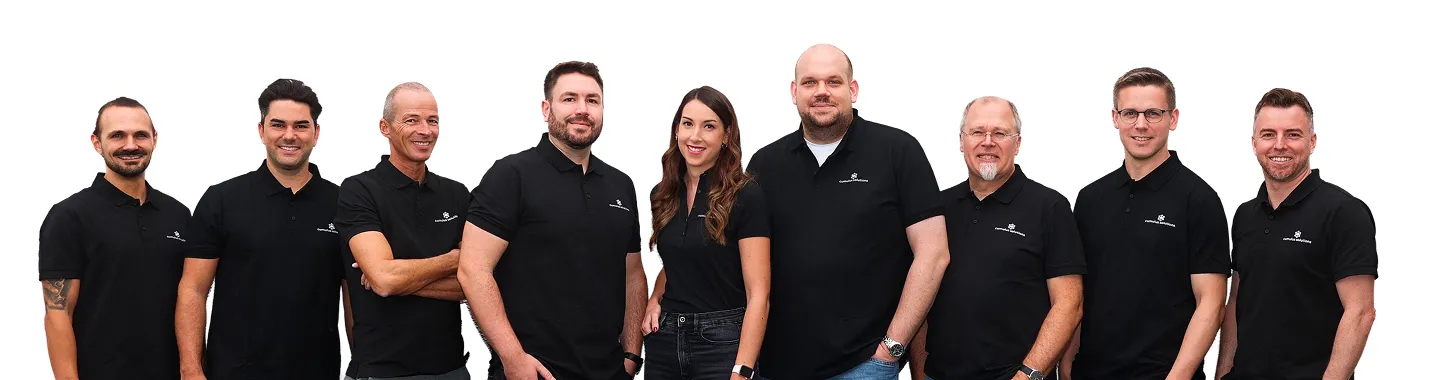 Group of nine people standing side by side wearing matching black polo shirts with a small white logo.