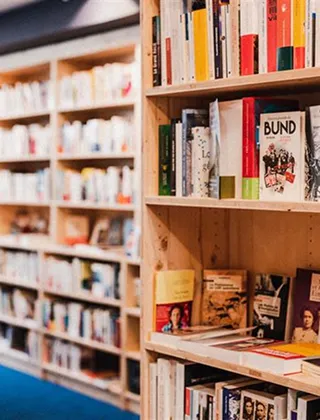 Gros plan sur des étagères en bois clair remplies de livres. Les livres du premier plan sont nets, tandis que les étagères en arrière-plan sont floues, donnant de la profondeur à l'image