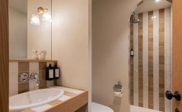 Un primer plano de un baño moderno con un lavabo empotrado ovalado y una ducha adyacente. Las paredes están cubiertas con azulejos de rayas verticales, que alternan entre blanquecino y beige/marrón claro