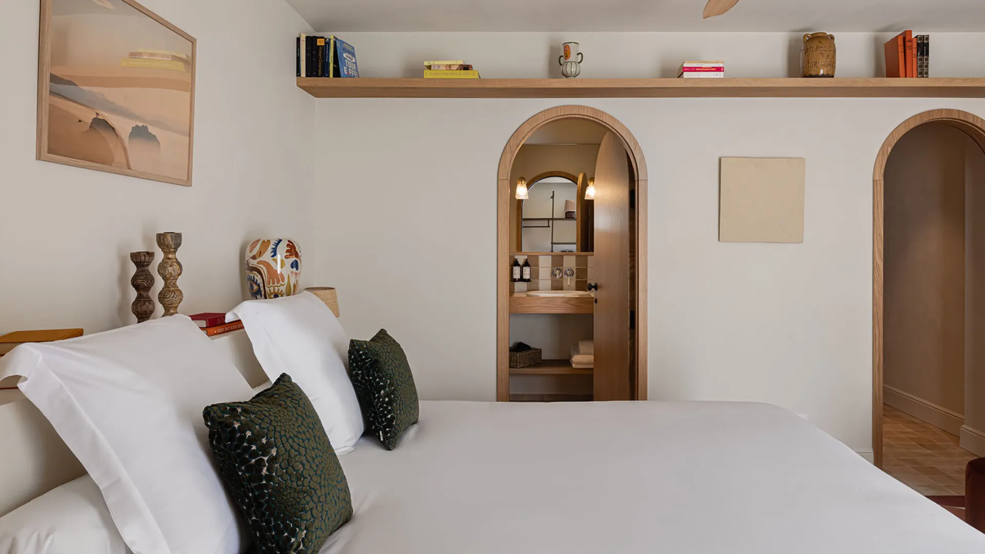 Chambre d'hôtel contemporaine avec lit blanc, tête de lit basse et arche décorative menant au couloir.