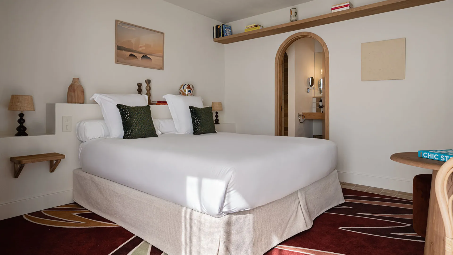 Intérieur de chambre d'hôtel moderne avec lit blanc, décoration minimaliste et arche vers la salle de bain.