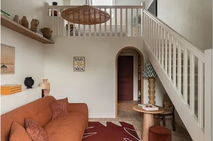 Salon bohème chic avec canapé terre cuite, mezzanine, et escalier blanc. Décoration avec suspensions en osier et poteries