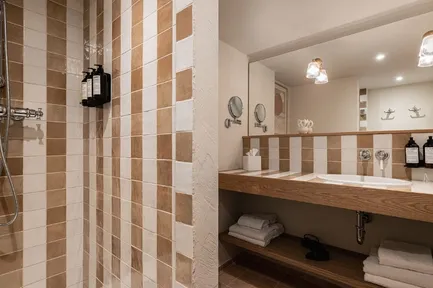 Salle de bain moderne et épurée avec un lavabo encastré, un grand miroir et un éclairage décoratif. La douche à l'italienne est carrelée de rayures verticales alternées en blanc et beige/marron clair