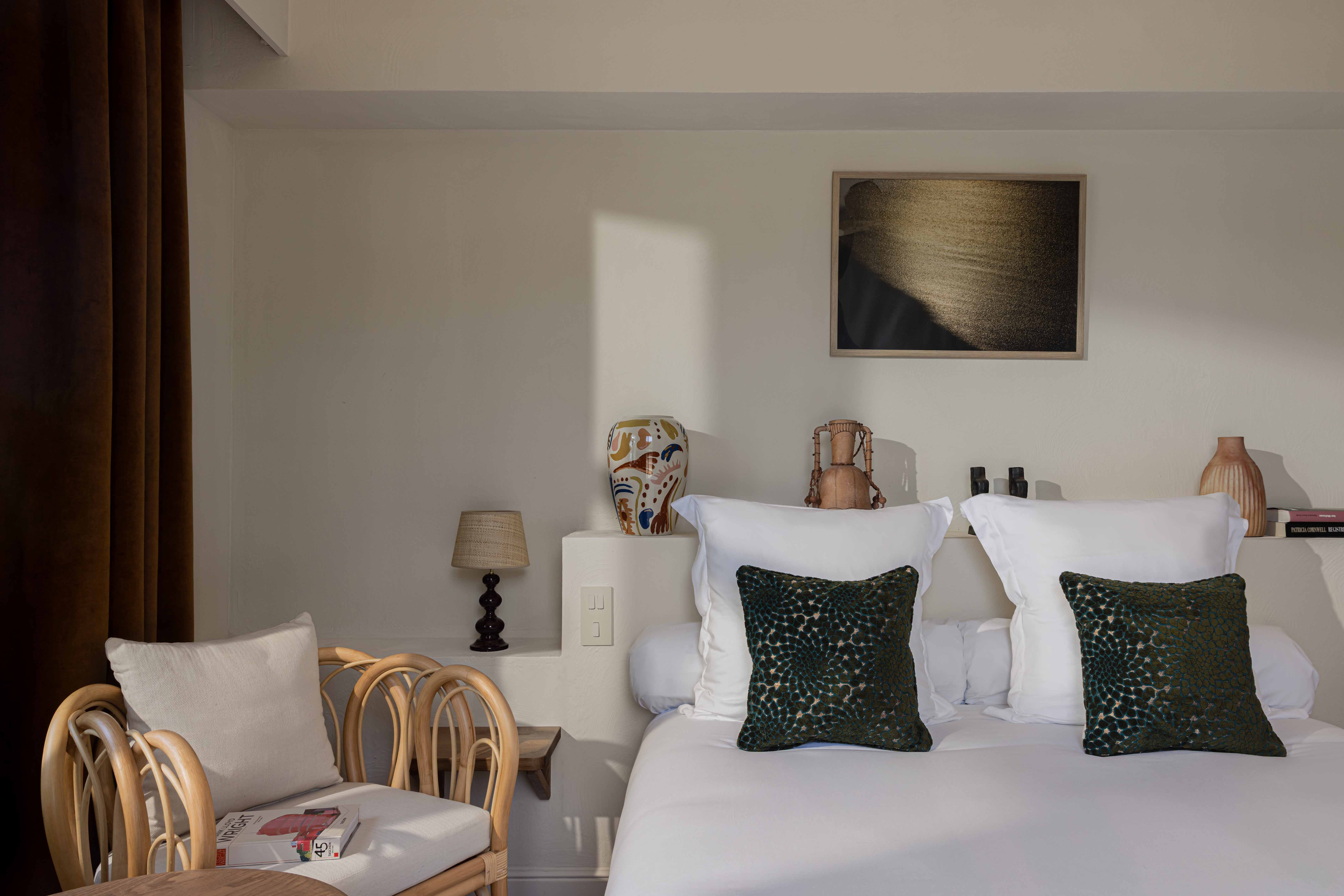 Salón de hotel moderno y cálido con tonos terracota y acentos naturales. La habitación incluye un sofá de tela texturizada, dos sillones de ratán y un gran televisor montado en la pared, y está iluminada por una lámpara colgante y una lámpara de pie de fibra natural.