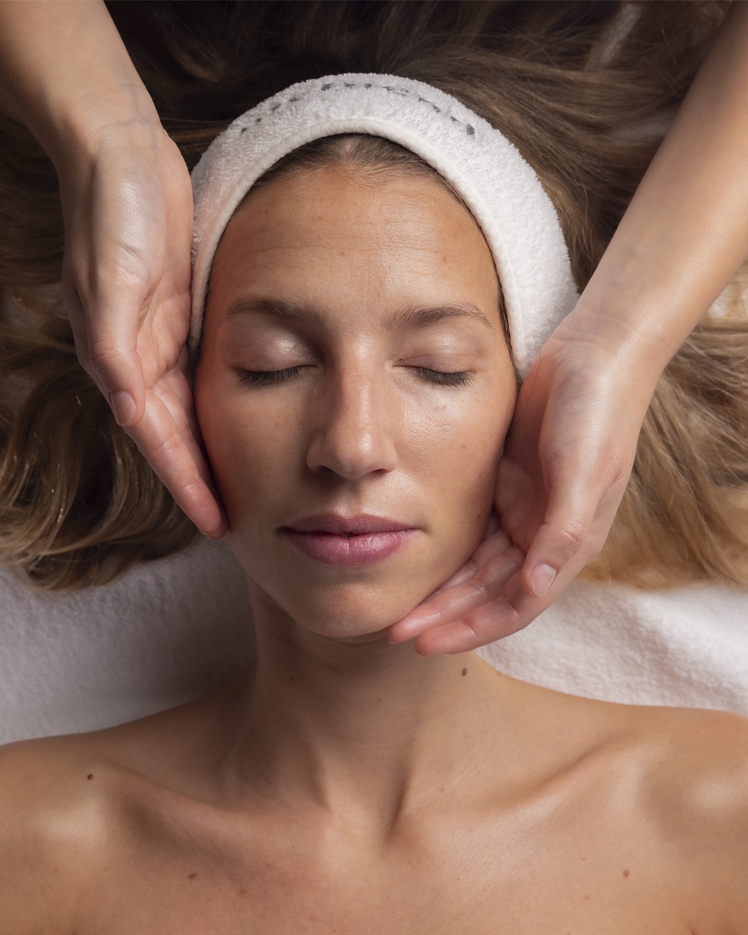 Gros plan et plan rapproché sur les mains d'un massothérapeute appliquant de la pression sur le dos nu d'une personne allongée, dans une ambiance de spa chaleureuse et tamisée.