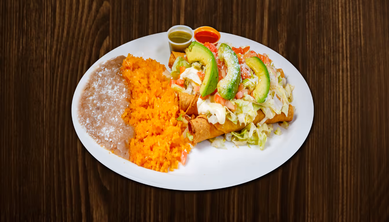White oval plate with two flautas topped with avocado slices, lettuce, sour cream, and diced tomatoes, served with Mexican rice, refried beans, and two small containers of green and red salsa.