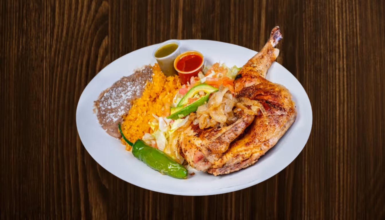 Plate with grilled chicken leg, Mexican rice, refried beans with cheese, grilled green chili, avocado slice, salad, and two small cups of red and green salsa on wooden table.