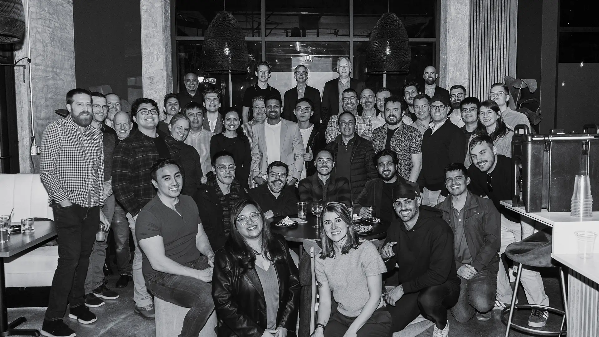 Large group of diverse people smiling and posing together in a modern indoor setting.