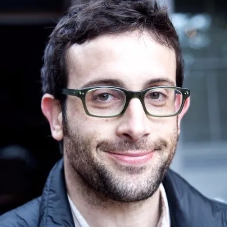 Smiling man with short dark hair, glasses, and light facial hair wearing a dark jacket.