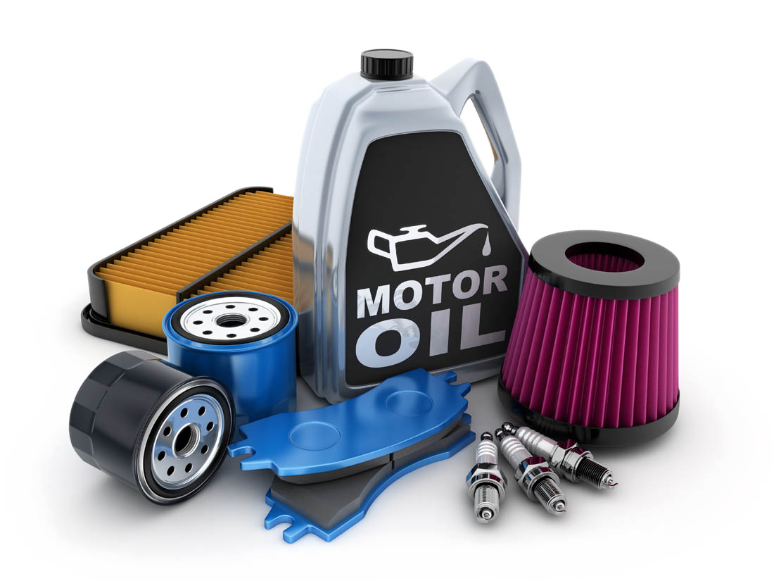 Car maintenance parts including a container of motor oil, air filters, oil filters, brake pads, and spark plugs arranged on a white surface.