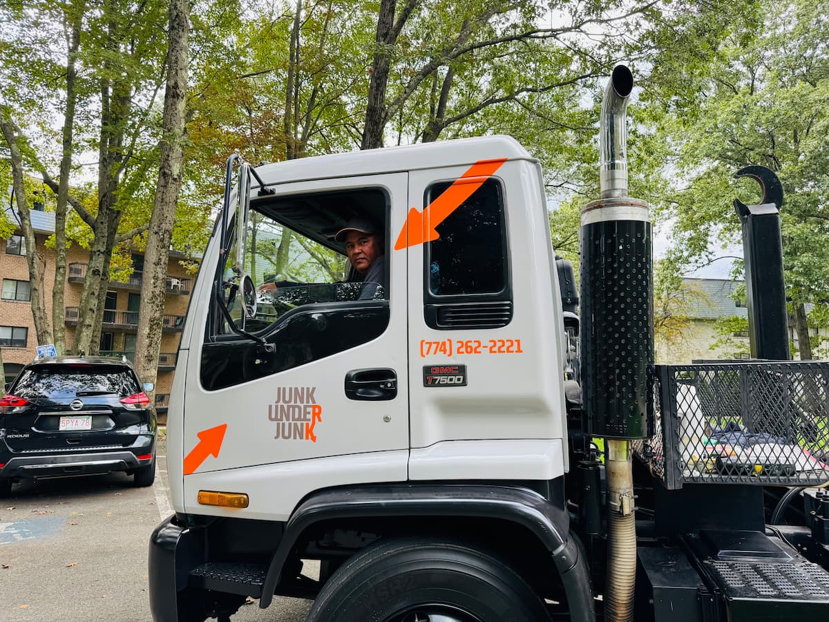 White truck with 'Junk Under Junk' logo and phone number, with a man sitting in the driver's seat.