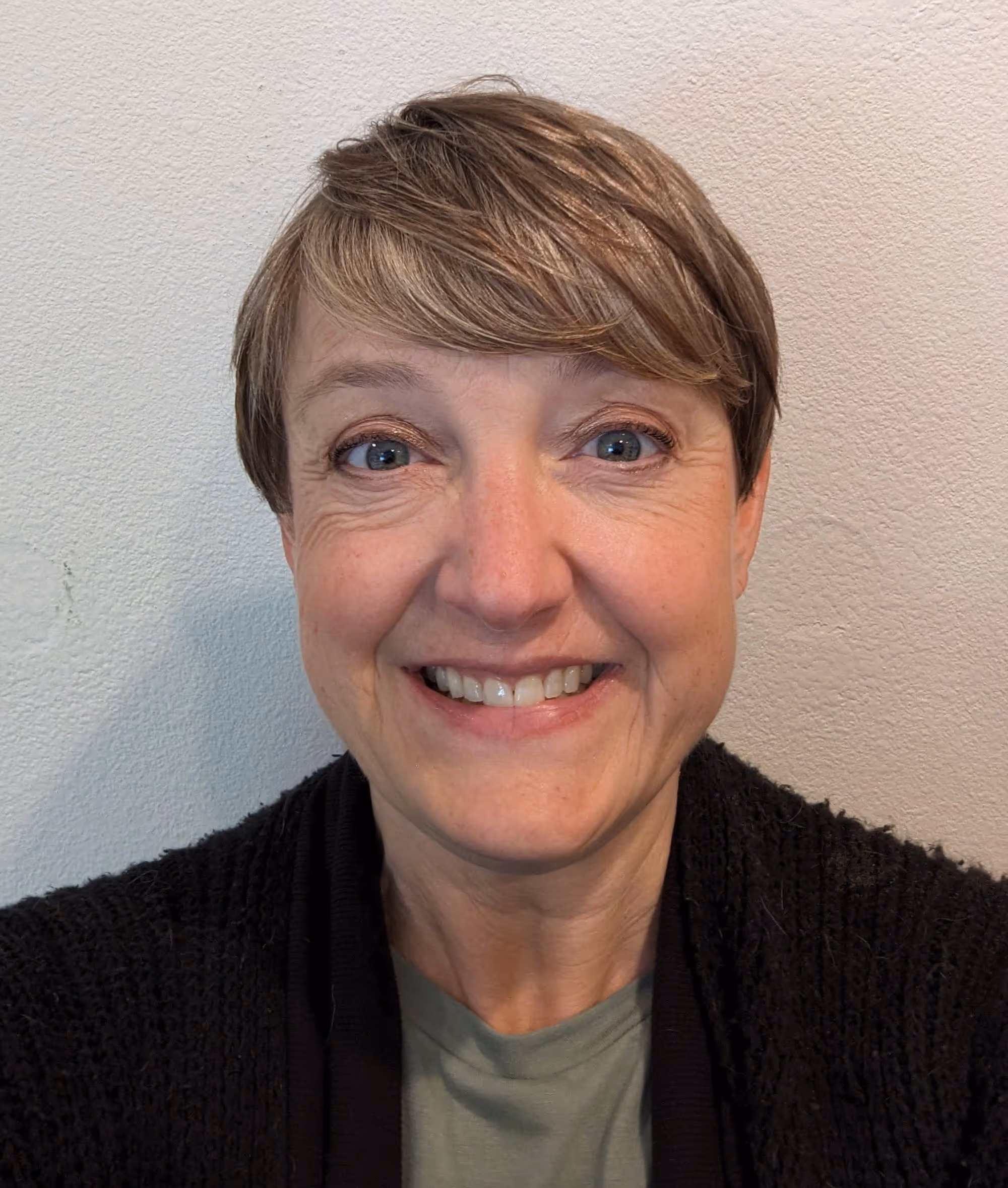 Close-up smiling headshot of a woman with short hair in front of a light-colored wall.