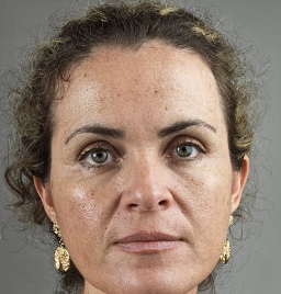 Middle-aged woman with curly hair and gold earrings looking directly at camera