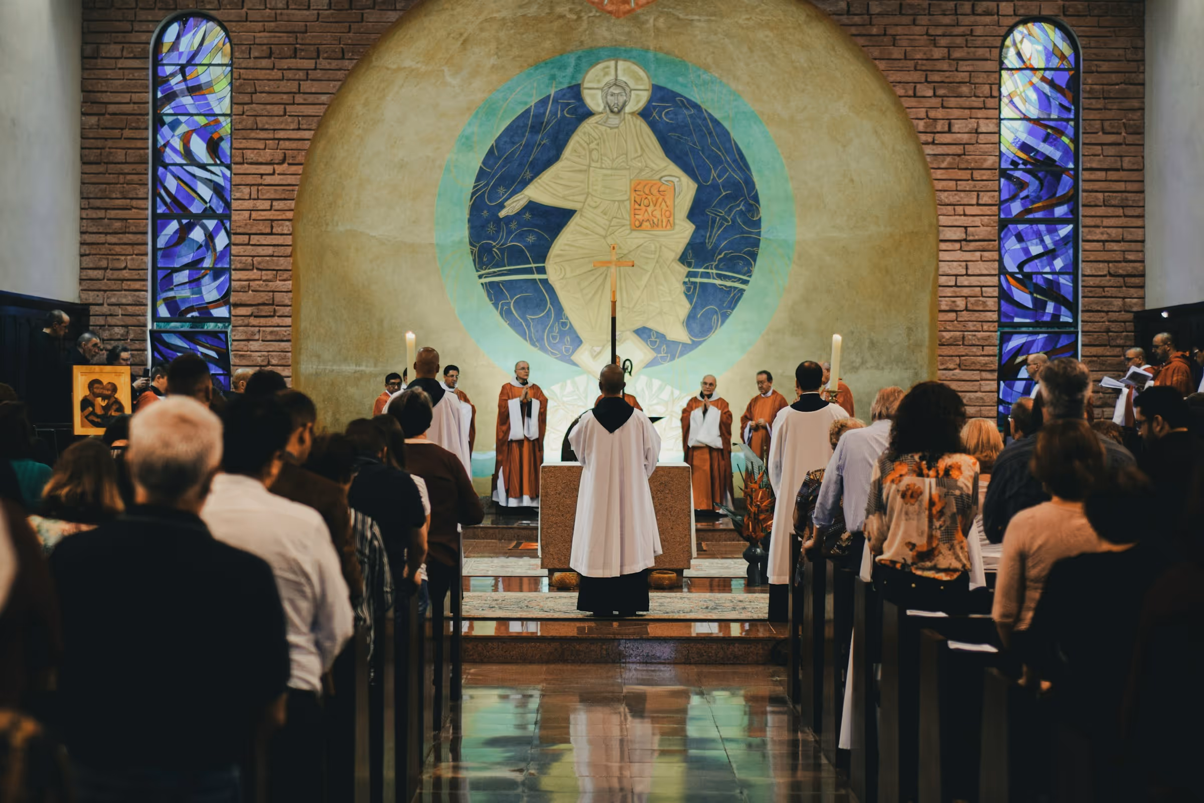 Worshipers standing during Mass inside a Catholic church with an icon of Jesus and stained glass in the background