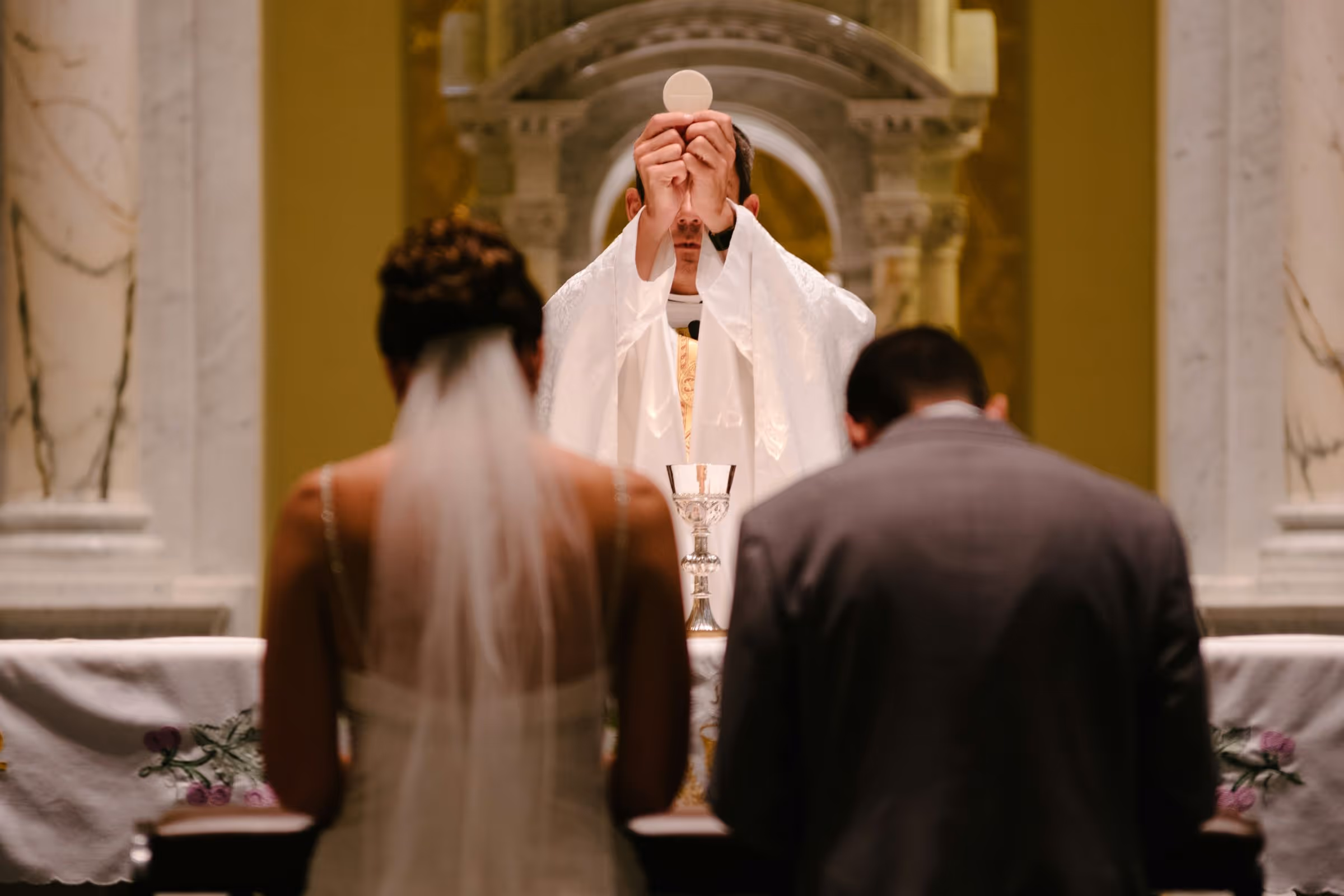Bride and groom kneeling in front of the altar during the Consecration at their Nuptial Mass