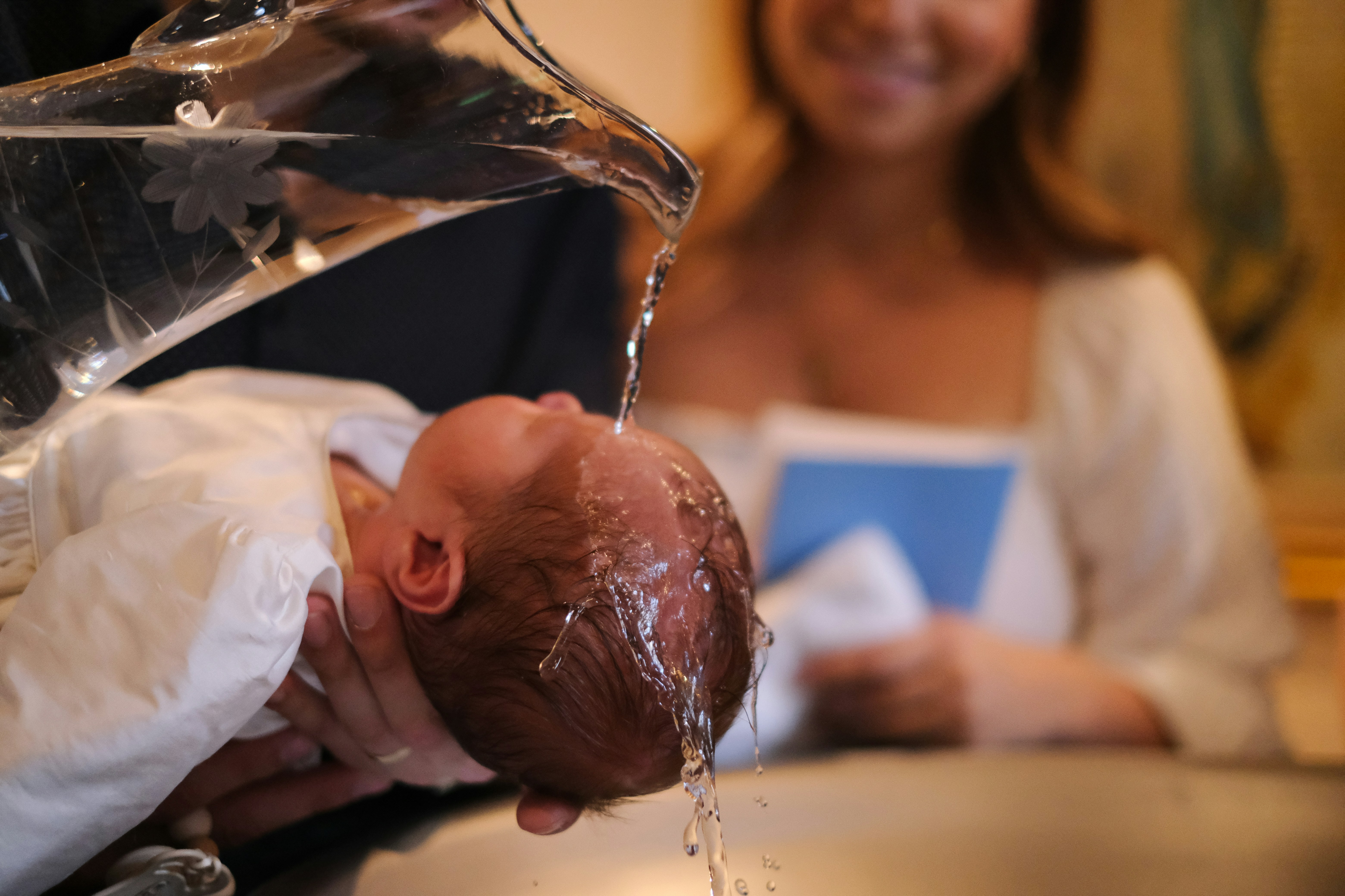 Infant receiving Christian baptism in a Catholic church with parents smiling in the background