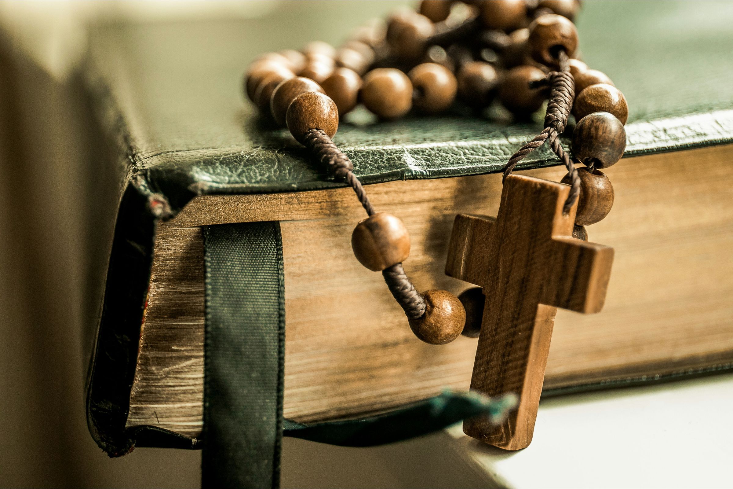 Close-up of wooden rosary beads resting on a worn leather Bible