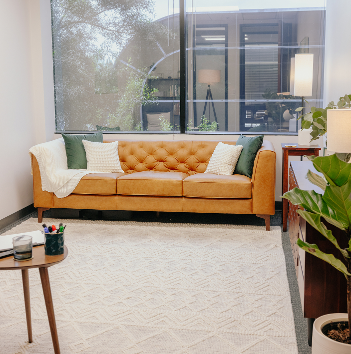 A photo of the office of Arbor Therapy in Carlsbad, California. A brown leather couch and inviting warm light in a calming space.