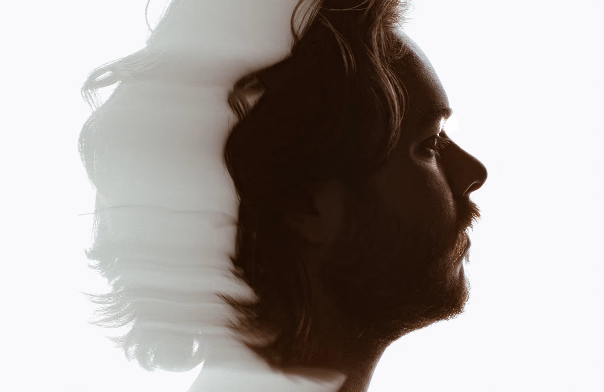Double exposure side profile of a man with long hair and beard blending into a translucent hair silhouette on a white background.