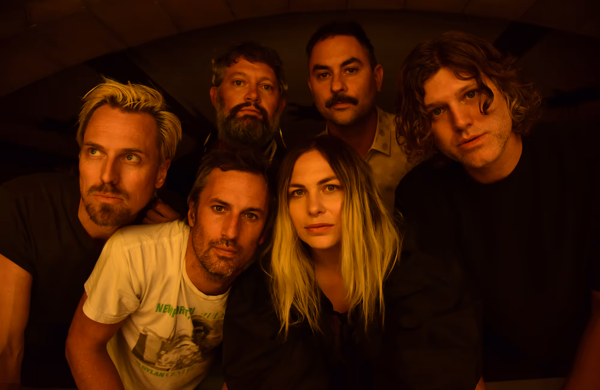 Band promo photo: The Head and the Heart. Portrait of six people with serious expressions in dim warm lighting, closely grouped and looking at the camera.