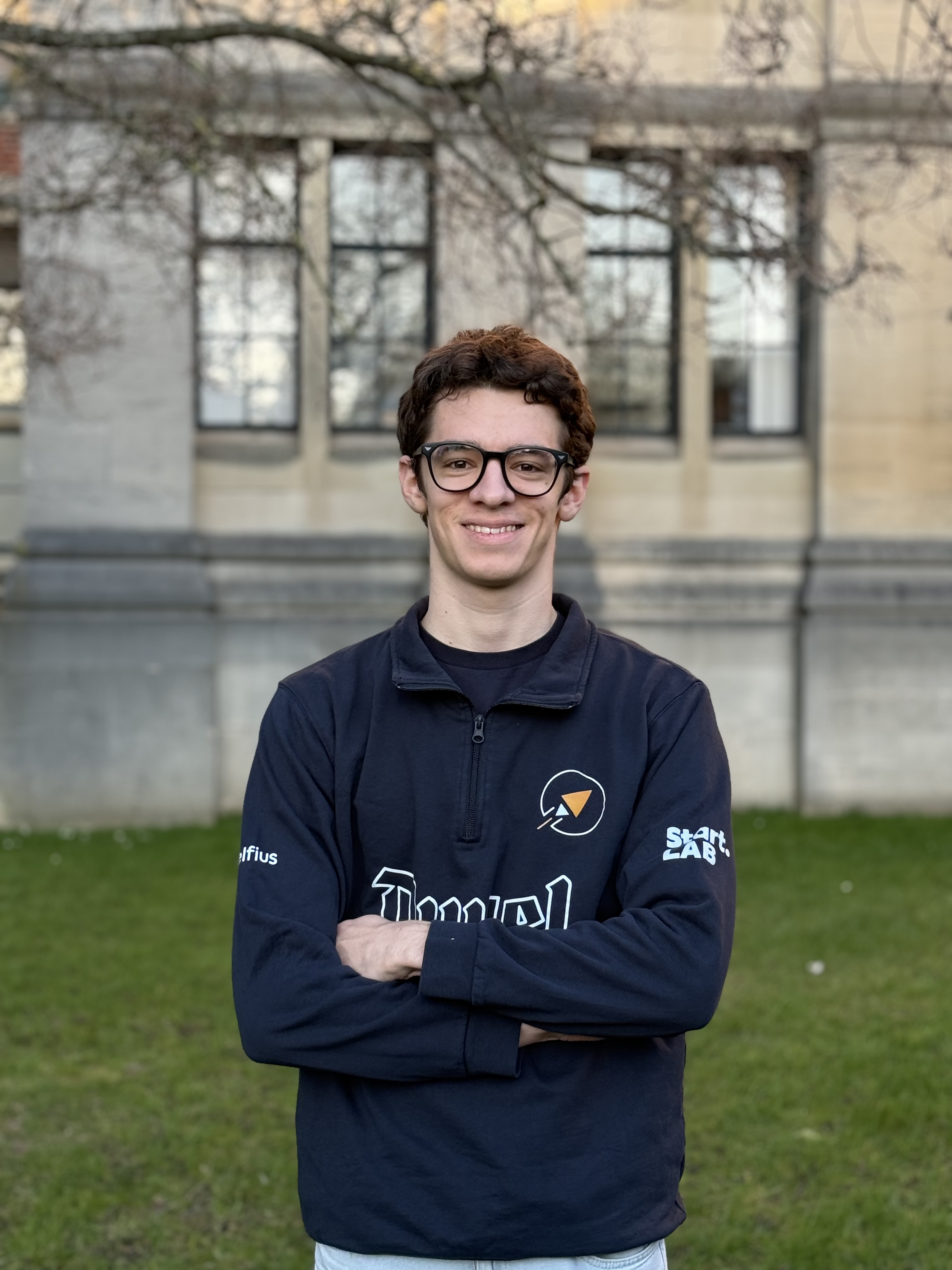 Jeune homme souriant avec des lunettes portant un costume clair sur un fond jaune.